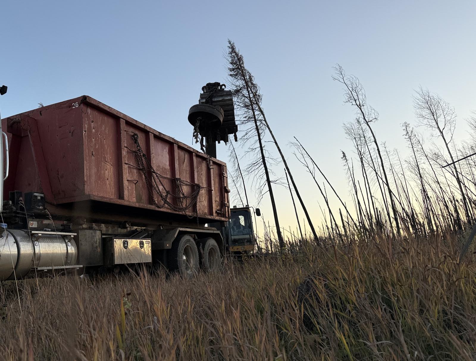Roll-off bin on a tandem truck being loaded by a material handler with a magnet attachment