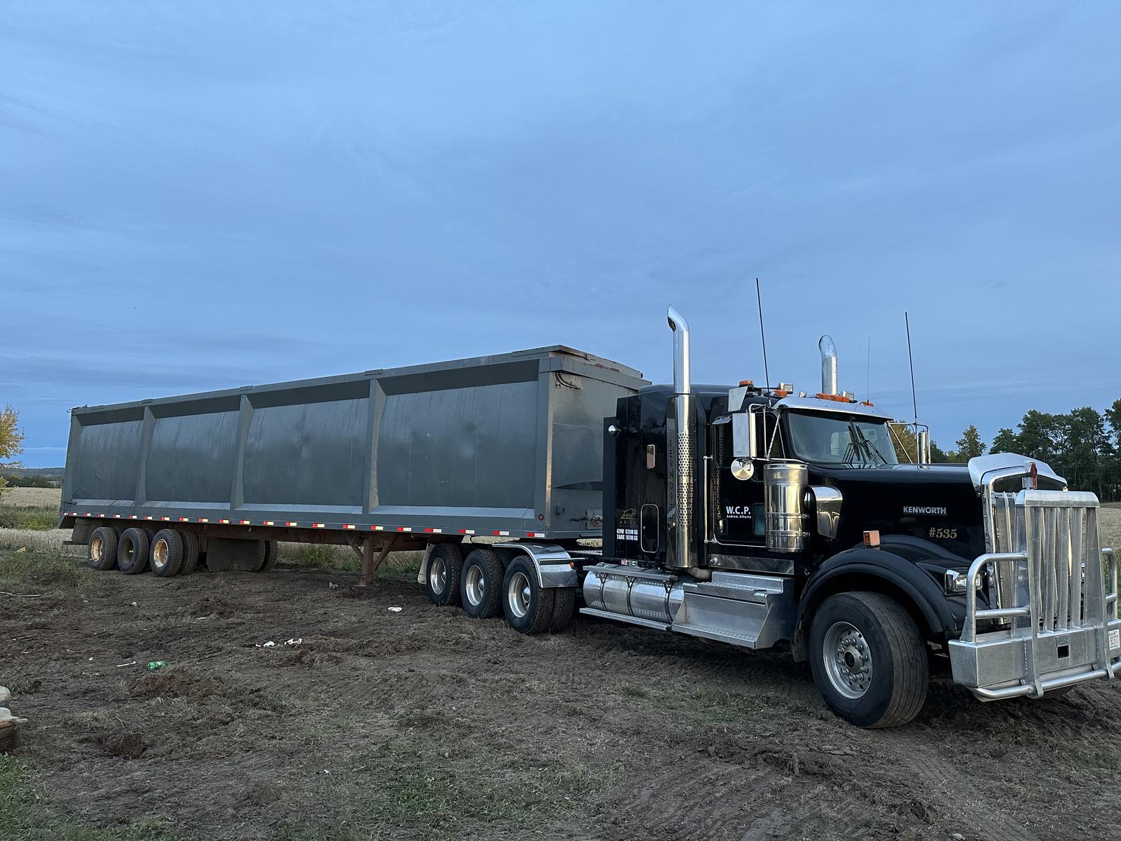 Kenworth Class 8 tractor coupled to a 53-foot open-top gondola trailer, staged at a field site